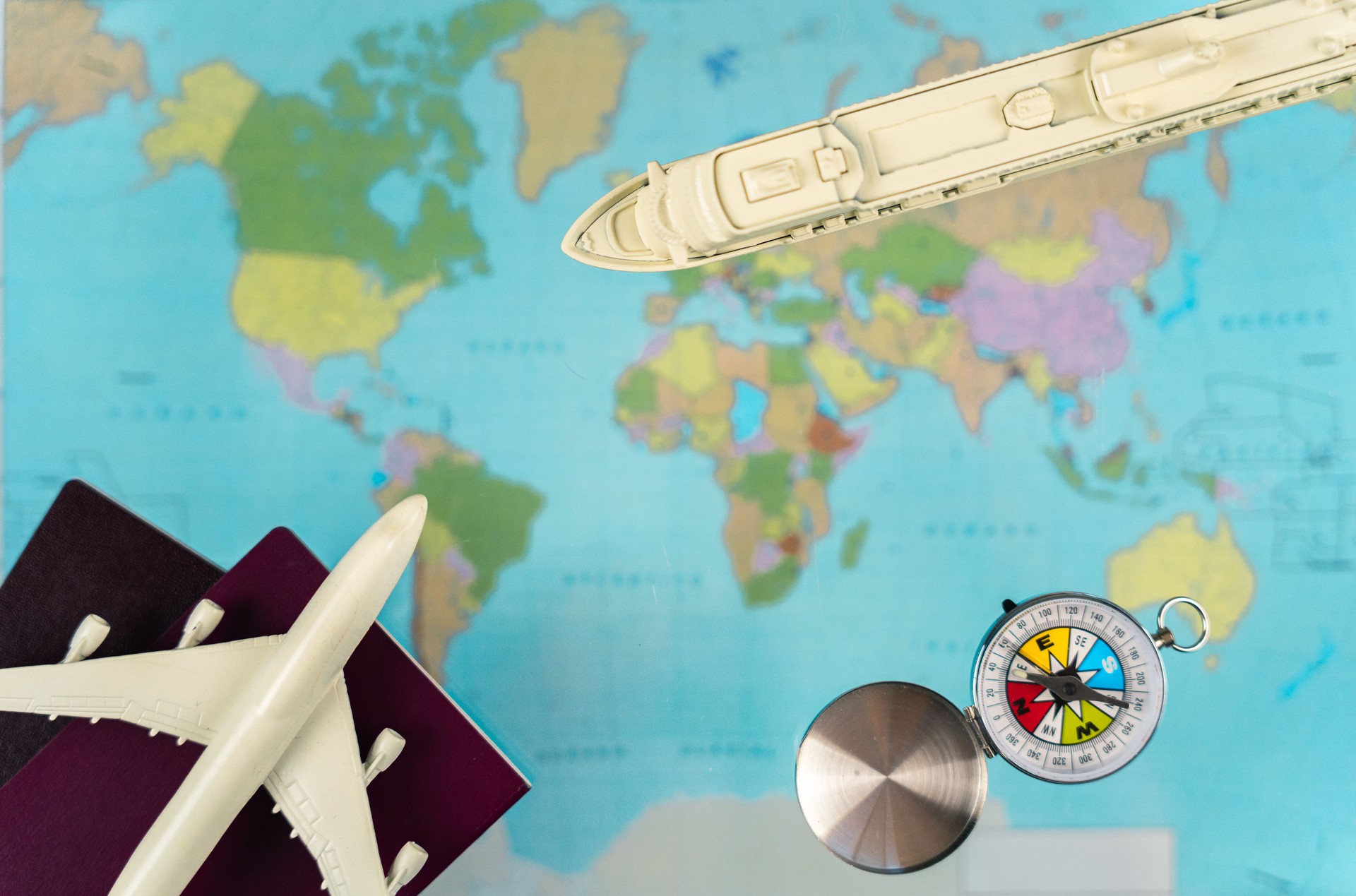 Travel planning setup with miniature airplane, passports, cruise ship, compass positioned across vintage world map surface